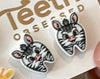 Dental earrings featuring panda, sloth, giraffe, and zebra tooth designs from Teeth Obsessed, displayed on a white background.