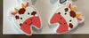Dental earrings featuring a llama, koala, and cow with tooth designs from Teeth Obsessed, shown on a display.