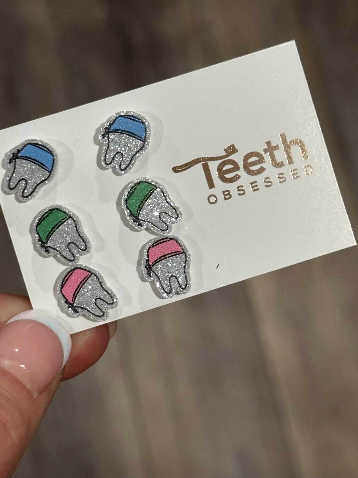 Teeth Obsessed dental earrings shaped like small teeth wearing scrub hats, perfect for dental professionals.
