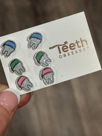 Teeth Obsessed dental earrings shaped like small teeth wearing scrub hats, perfect for dental professionals.