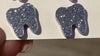 Purple dental earrings with tooth-shaped charms from Teeth Obsessed, displayed on a hand mirror.
