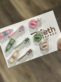 Pink dental earrings featuring miniature toothpaste, toothbrush, and floss designs from Teeth Obsessed, perfect for dental enthusiasts.