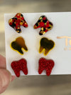 Red dental earrings from Teeth Obsessed featuring glittery tooth-shaped design on a white background.