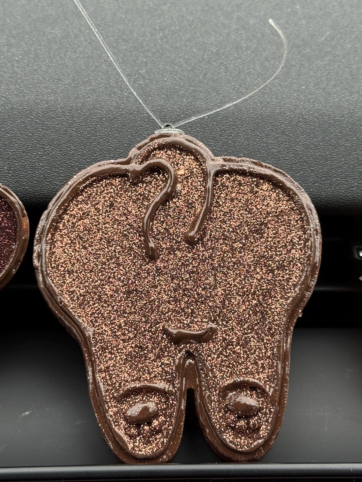 Teeth Obsessed vanilla-brown doggie tooth car freshener vent freshie hanging in a vehicle interior.