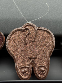 Teeth Obsessed vanilla-brown doggie tooth car freshener vent freshie hanging in a vehicle interior.