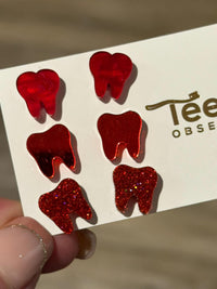 Red swirl earrings from Teeth Obsessed with Valentine-themed design, featuring thin, curved red swirl patterns on shiny metal.